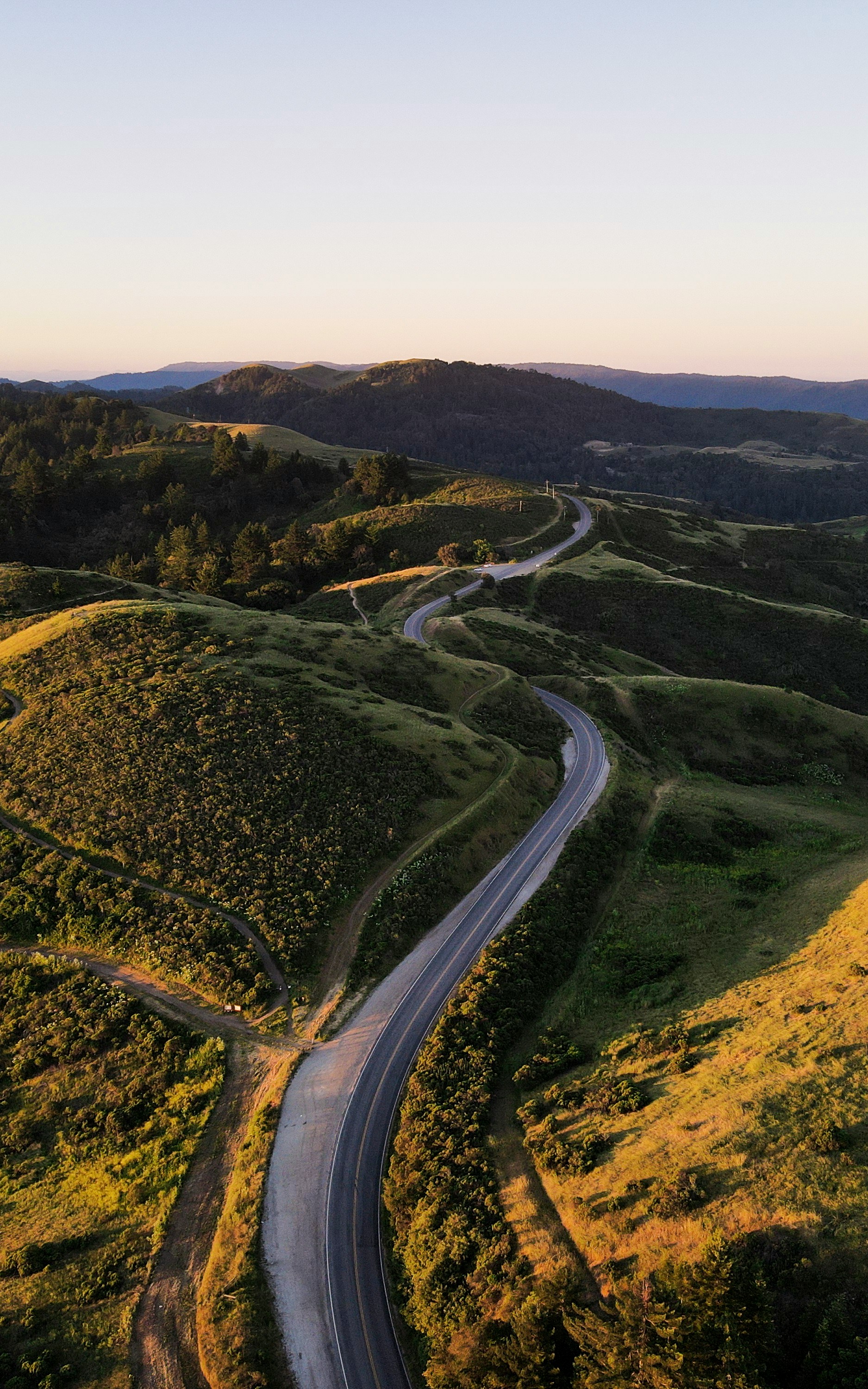 A winding road through rolling green hills at sunset